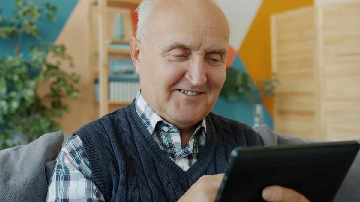 Signore anziano che usa un tablet seduto sul divano di casa
